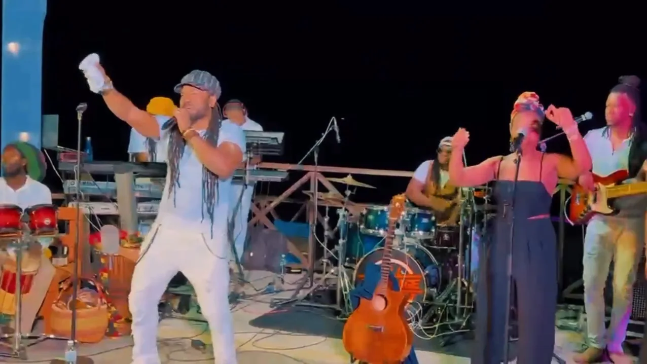 Hezron raising a cup mid-song on the Sky Beach stage, backing vocalists and a drum kit behind him