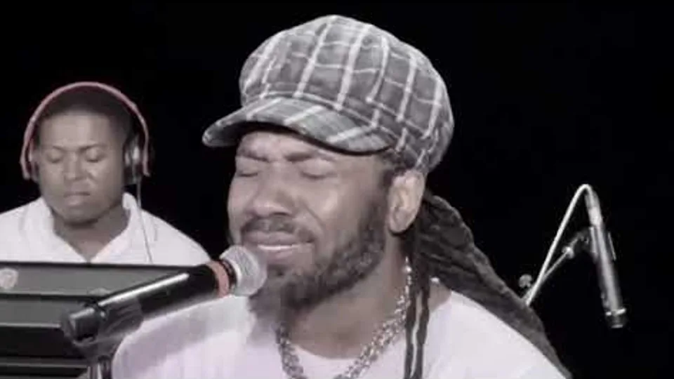Hezron singing with his eyes closed into a microphone, a keyboardist in headphones behind him