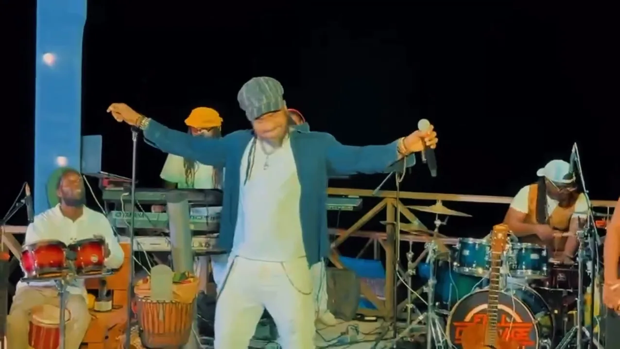 Hezron on the Sky Beach stage at night, arms outstretched, with a full band behind him